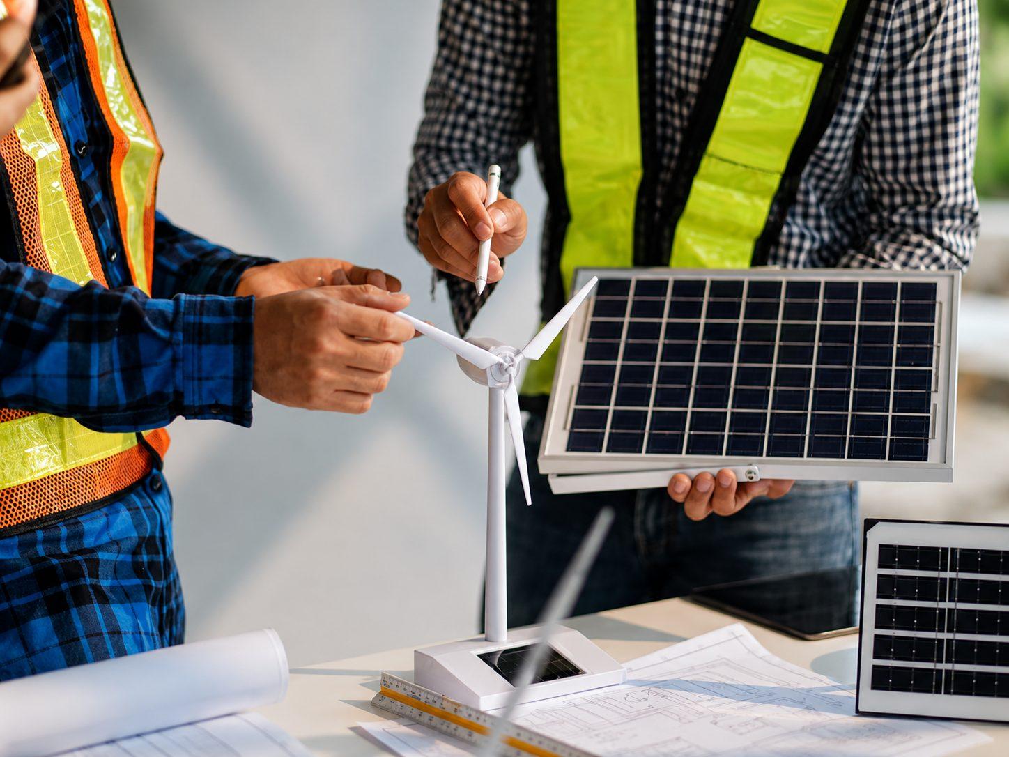 Two engineers reviewing a wind turbine and solar module